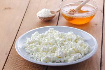 Cheese, fresh cottage cheese in a white plate, wooden spoon, cottage cheese and honey on a wooden background, sour cream in a wooden spoon, dairy products on a natural background, retro style