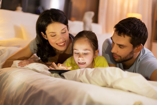 family with tablet pc in bed at night at home