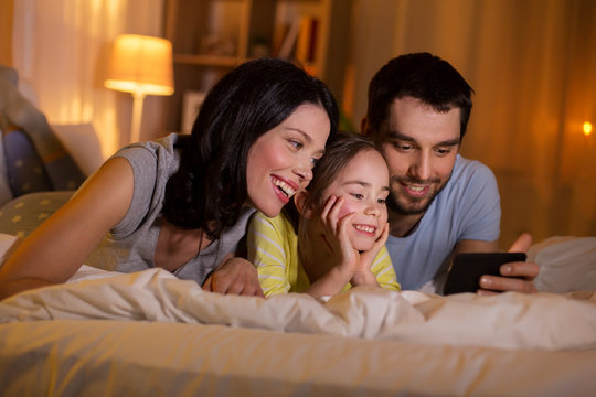 happy family with smartphone in bed at night