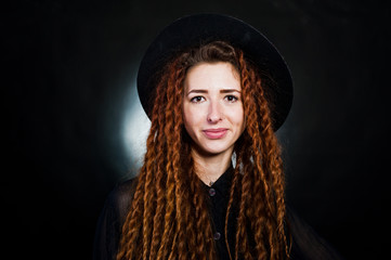 Studio shoot of girl in black with dreads and hat at black background.