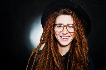 Studio shoot of girl in black with dreads, hat and glasses at black background.