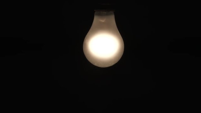 Frosted incandescent light bulb turns on, off and flickers transition to black, seamless looping.