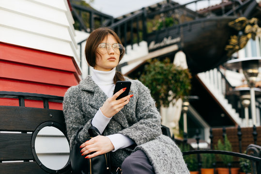 woman sitting on a bench in the park with a phone in hands - Powered by Adobe