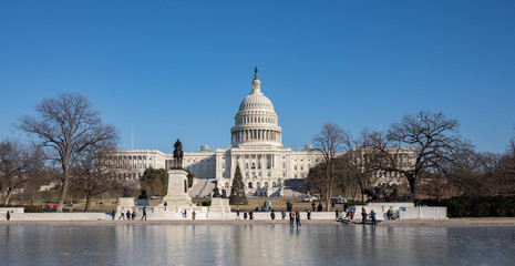 The Capitol Building in Washington, D.C. in the winter and the reflection pool is frozen with tourists walking on it.