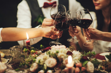 People clang glasses sitting at dinner table in sparkling lights