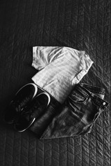 Black and white high angle view of folded jeans, t-shirt and tennis shoes on bed - 195549710