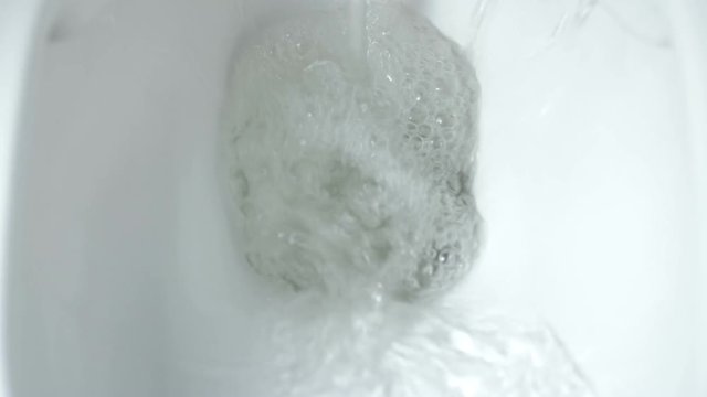Close-up top view of yellow pee flushing down the toilet. Directly above shot of urine being flushed down the toilet with water