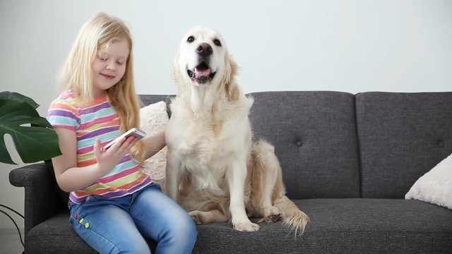 devices in the lives of children. A little girl does selfie with her dog on a smartphone. Location - sofa in the living room.