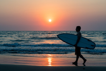 surfer walking on beach at sunset - obrazy, fototapety, plakaty