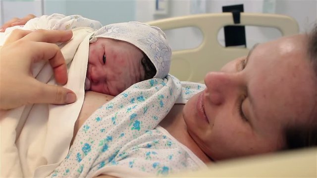 a newborn baby lies on the breast of a happy mother in the hospital. The first minutes of life.