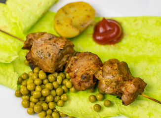 Fried meat on green pita bread with spinach and peas and baked potatoes.