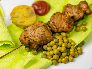 Fried meat on green pita bread with spinach and peas and baked potatoes.