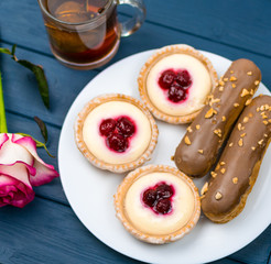 Different cakes with custard and cream and berries on a white plate with tea in the background.