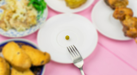 The concept of starvation, bulimia. A pea on a fork surrounded by blurry dishes.