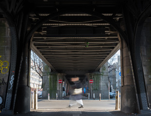 blurred pedestrian under a subway bridge