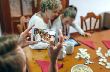 Grandmother and granddaughter play a game on the tablet while the mother takes a photo with the smartphone. Selective focus on smartphone in foreground