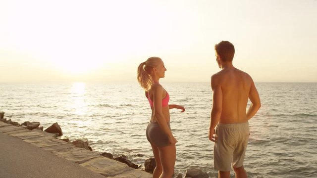 SLOW MOTION, COPY SPACE: Young girlfriend and boyfriend illuminated by setting summer sun celebrate success with a high five. Couple on holiday high fives after fun jog at the picturesque seaside.