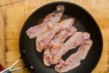 Streaky bacon cooking in the frying pan