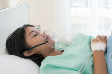 Asian young woman patient receiving oxygen mask lying on a hospital bed.