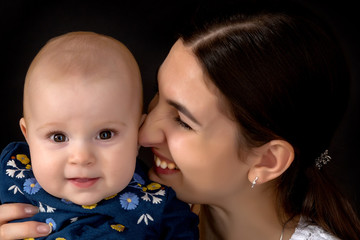 Happy young mother with her daughter on her hands on a black bac