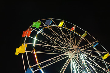 Part of a ferris wheel with brightly painted seats against a night sky