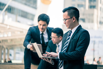 Group of  Asian business men working outdoor with computer devices. Technology and teamwork concept