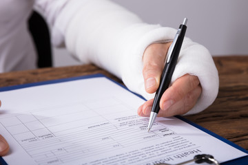 Man With Broken Arm Filling Health Insurance Claim Form