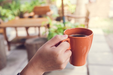 Closeup image of a hand holding a brown cup of hot coffee in the morning with blur background