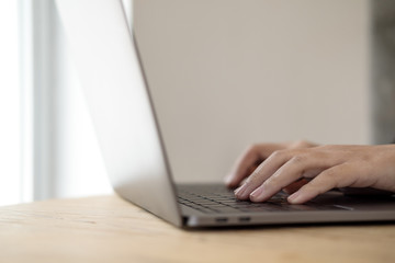 Closeup image of hands working and typing on laptop keyboard on wooden table