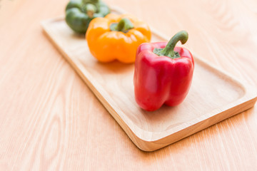 Colorful bell peppers on wooden plate on the wood table