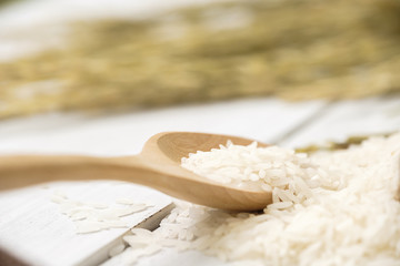 A wooden spoon filled with rice placed on wooden background.