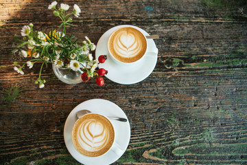 Top view of two cups of coffee and a vase of flowers on a wooden table. A photo means a meeting or a date.