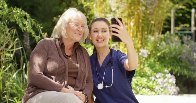 4K Senior lady posing for selfie with care worker in the garden of retirement home