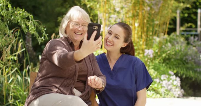 4K Happy senior lady posing for selfie with community nurse in the garden at home