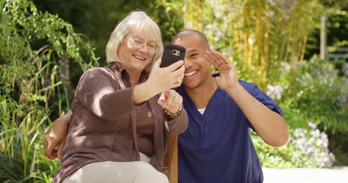 4K Happy senior lady sitting in the garden, posing for selfie with home care worker