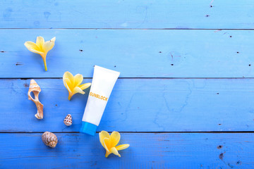 Beach accessories. Blank sunblock/moisturizer, plumeria flowers, sea shell on blue wooden background