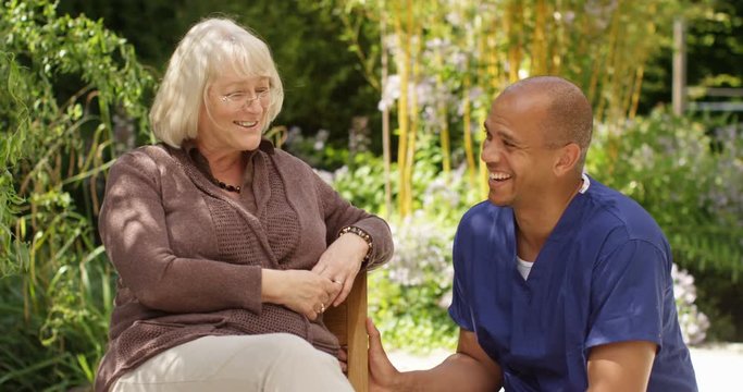 4K Cheerful senior lady & health care assistant relaxing in the garden, laughing & chatting