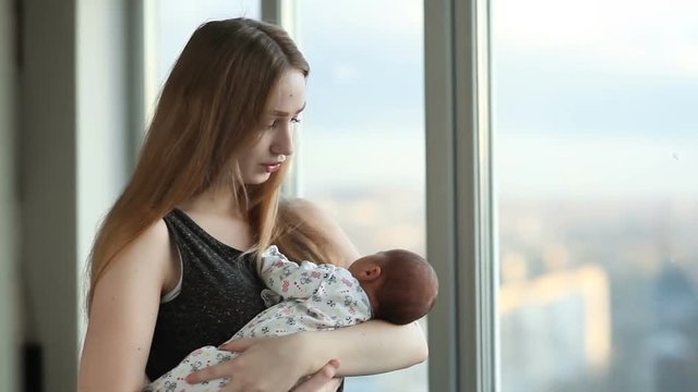 Young mother with a newborn daughter standing near the window