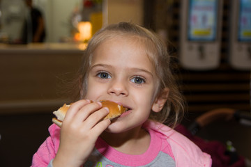 Cute little blond girl eating a hamburger