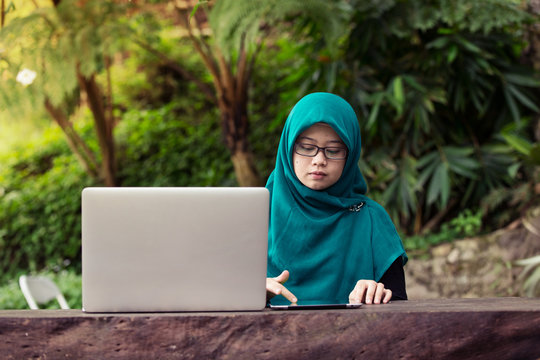A hijab muslim woman using laptop on wooden table in the outdoor cafe