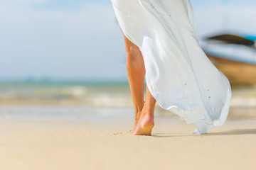 Fototapeta na wymiar White pareo woman legs walking on tropical beach vacation. Closeup of barefoot female young adult lower body relaxing in ocean water on summer holiday travel wearing cover-up beachwear.