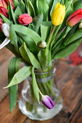 Flower background: bouquet of colorful tulips in a glass vase on a natural wooden background, postcard, mocap for mother's day greetings, international women's day