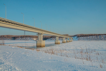 a bridge across a river covered with ice and snow on winter sunny day