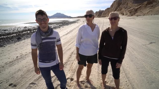 Three generations, grandmother, mother, son all give the finger to the camera in a playful way on a sandy beach.