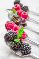 Fresh berries on steel spoons on white marble background 