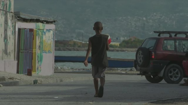 Kid Walking Towards Fishing Boat and Sea, Street in Cité Soleil, Port-au-Prince, Long Shot