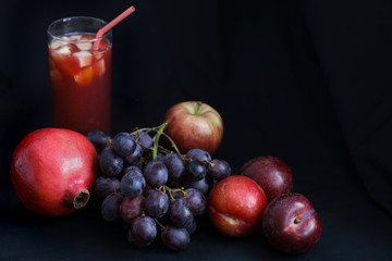 Dark Food - Chiaroscuro pomegranite, grapes, apple and plums with fruit punch on dark backround with copy space