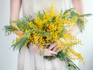 Bouquet of bright, yellow flowers in the hands of a young woman in a white dress. Wedding preparations - Powered by Adobe