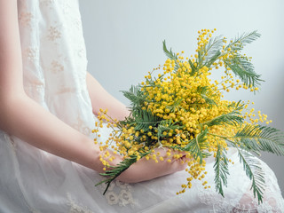 Bouquet of bright, yellow flowers in the hands of a young woman in a white dress. Wedding preparations