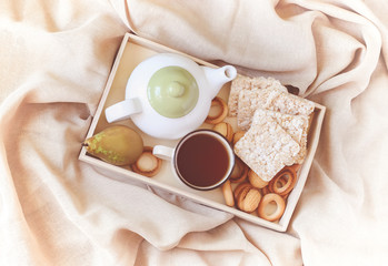 Breakfast in bed in a wooden tray with pear, bisquits, sweet cookies, teapot and cup of tea.